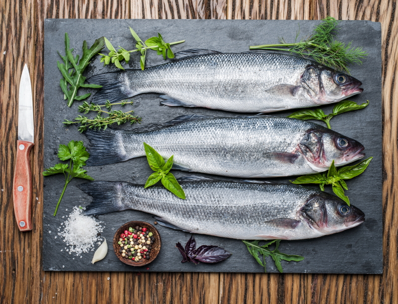 Three fish - seabass on a graphite board with spices and herbs.