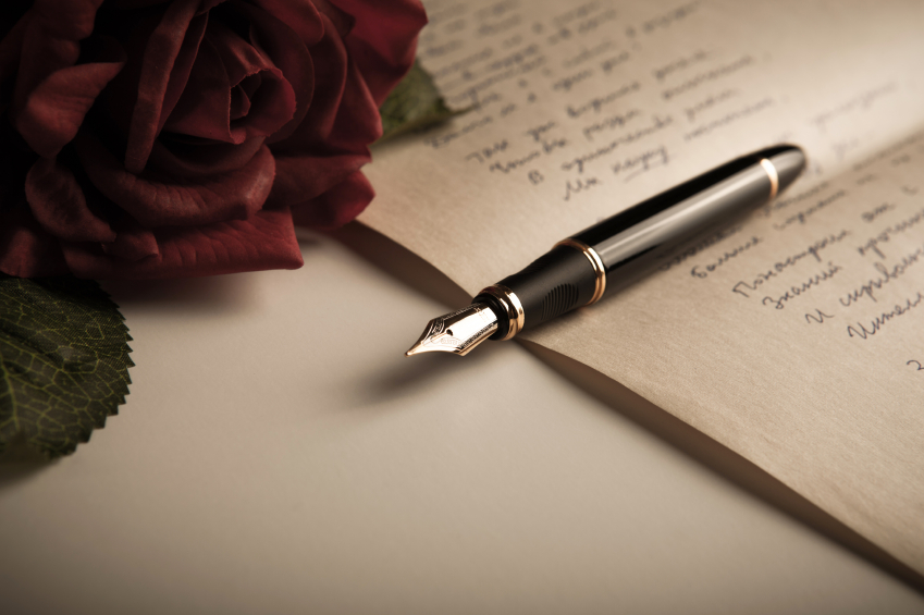 A close up of a fountain pen and rose, laid out on a sheet of paper 